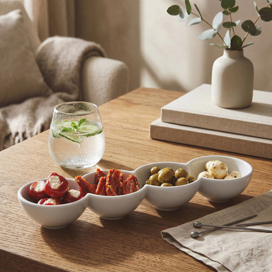 Four-section white serving dish with olives, tomatoes and snacks styled on a wooden table