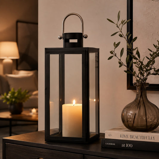 Black rectangular candle lantern with clear glass panels and lit pillar candle styled on a side table
