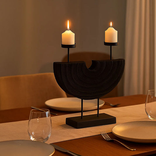 Black double candle holder with curved sculptural frame and two lit pillar candles on a dining table