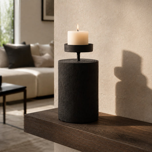 Black wooden candle holder with cylindrical base and single lit pillar candle on a side table