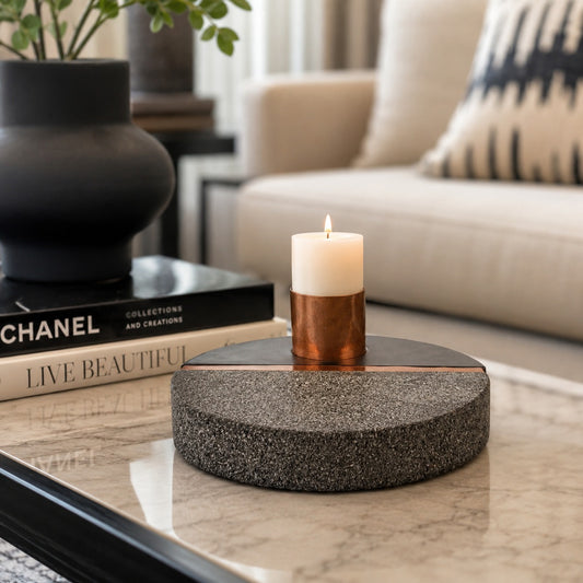 Black and grey round candle holder with a small lit candle displayed on a marble coffee table