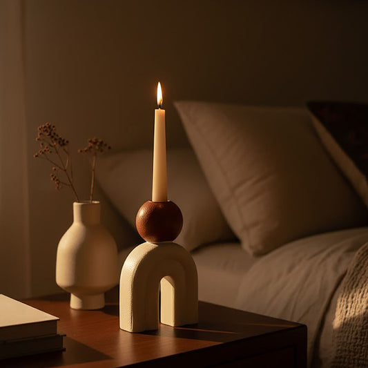 Cream sculptural candle holder with brown accent and single lit taper candle on a side table