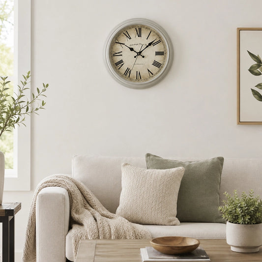 Grey plastic wall clock above sofa with neutral cushions and plant