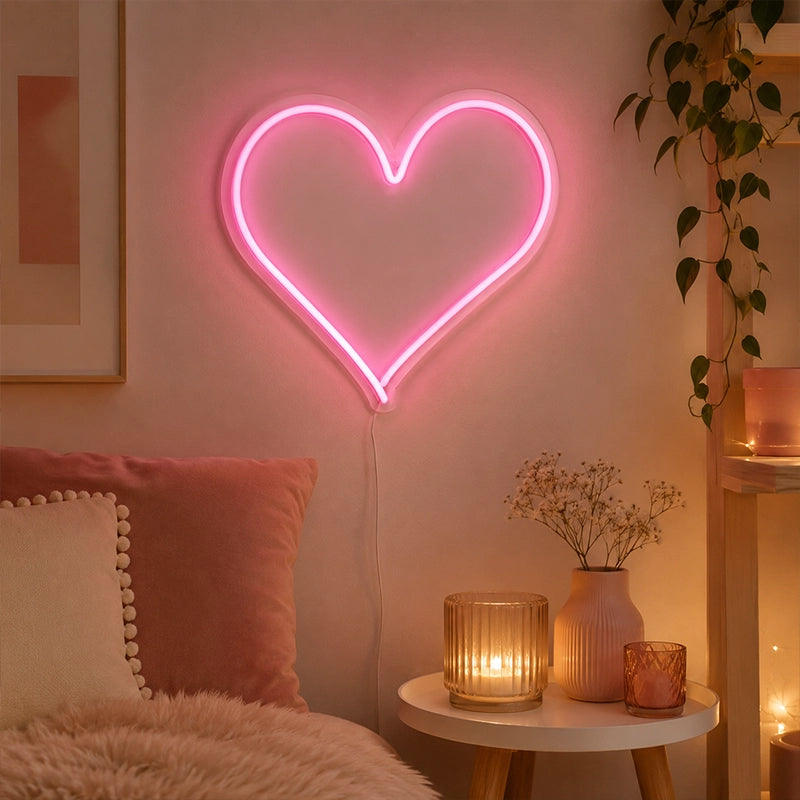 Pink heart LED neon light on bedroom wall beside bedside table with candles and plant