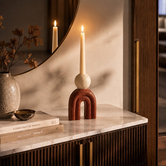 Red arch-shaped candle holder with white taper candle styled on a marble console table