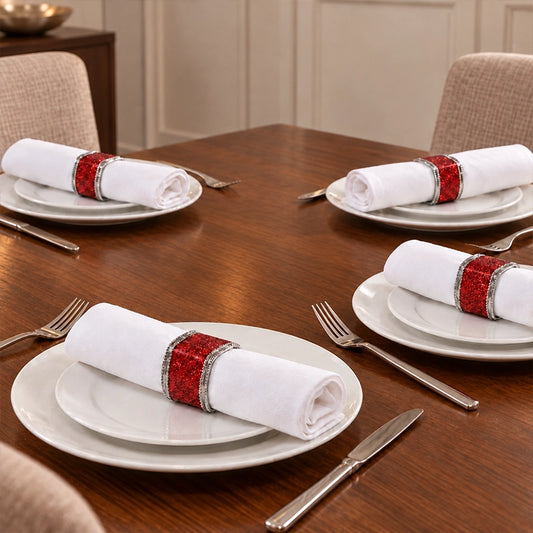 Red glitter napkin rings with silver trim holding white rolled napkins on dinner plates at a formal dark wood dining table