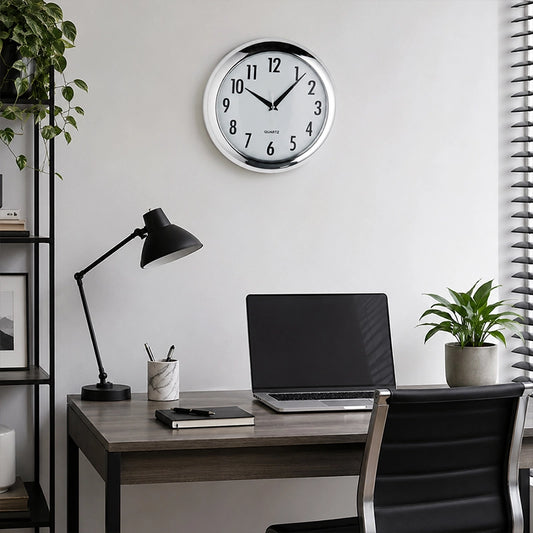 Silver plastic wall clock above home office desk with black lamp and laptop