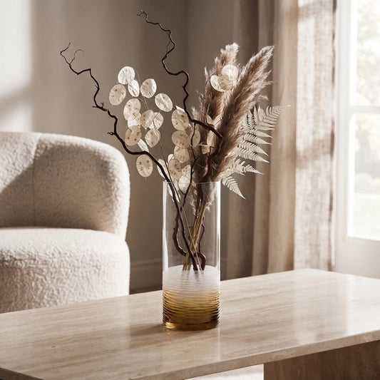 Small cylindrical glass vase with decorative dried stems displayed on a wooden table