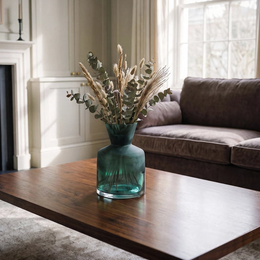 Small green glass vase with dried botanical stems displayed on a wooden coffee table