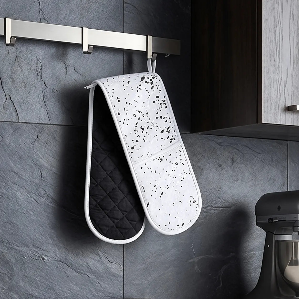 Black and white double oven gloves hanging in a modern kitchen for heat protection