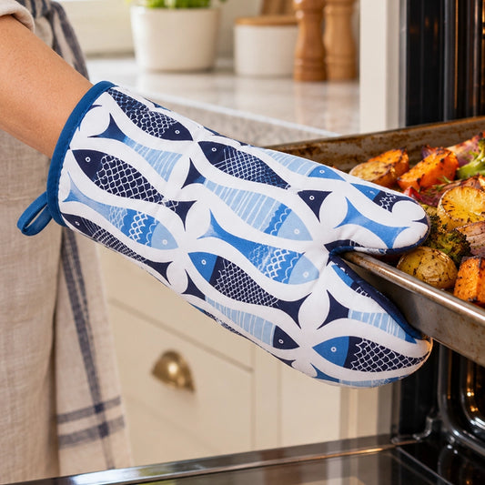 Blue cotton single oven glove with fish print pattern used to pull a baking tray from the oven