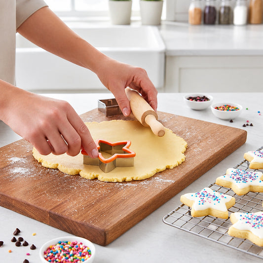 Hands pressing a metal star cookie cutter into rolled dough on a wooden cutting board