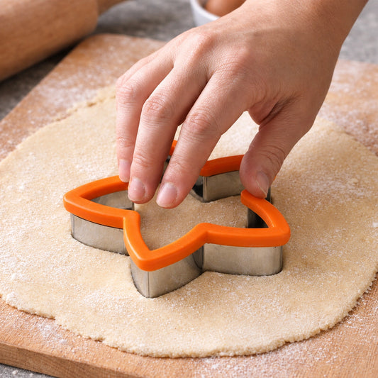 Hands pressing an orange star cookie cutter into rolled sugar cookie dough