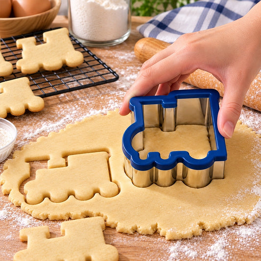 Hand pressing a blue rim train cookie cutter into dough with train shaped cookies cooling on a rack