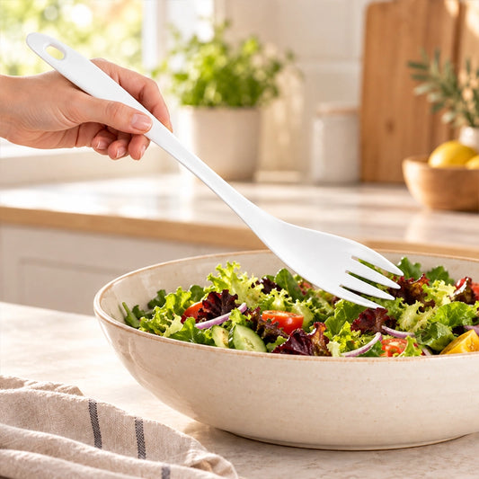 White melamine fork held in hand while tossing a fresh green salad in a serving bowl
