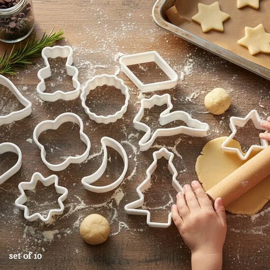 10 piece white plastic cookie cutter set in assorted shapes on rolled dough with freshly cut cookies on a wooden table
