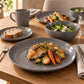 Grey 12-piece stoneware dinner set with plate, side plate, bowl and mug served with roast chicken and vegetables on a wooden table