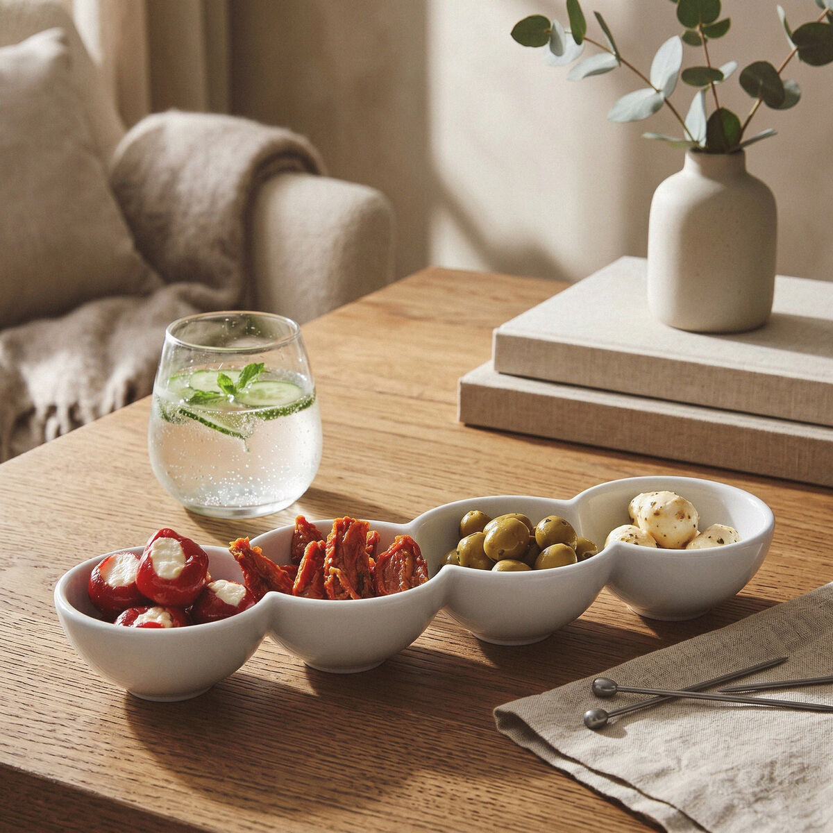 Four-section white serving dish with olives, tomatoes and snacks styled on a wooden table