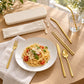 6-piece gold cutlery set with beige travel box, fork, knife and spoon laid beside a pasta and tomato dish on a wooden table