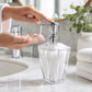 Clear acrylic lotion dispenser with pump being used beside a bathroom sink