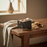 Black square candle holder with gold veining and a lit candle styled on a wooden table