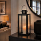 Black metal and glass candle lantern with handle and lit pillar candle displayed on a console table
