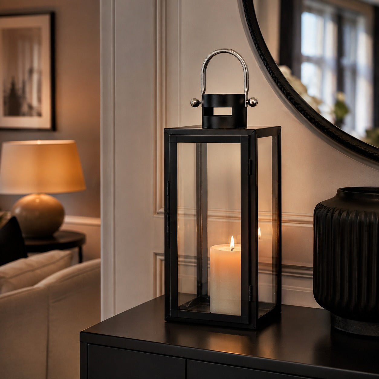 Black metal and glass candle lantern with handle and lit pillar candle displayed on a console table