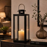 Black rectangular candle lantern with clear glass panels and lit pillar candle styled on a side table