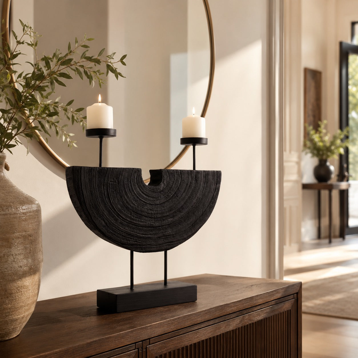 Black sculptural double candle holder with two lit candles displayed on a wooden console table