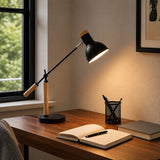 Black table lamp with wooden arm on desk beside notebook and window