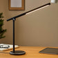 Black touch desk lamp with slim LED bar on wooden desk beside tablet and glasses
