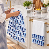 Blue and white fish-print cotton kitchen tea towels hanging on white shaker cabinet doors