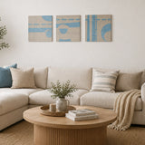 Set of three blue and cream abstract wall art panels with geometric shapes above a neutral sofa