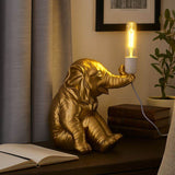Gold elephant table lamp with glowing bulb on side table beside open book