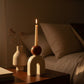 Cream sculptural candle holder with brown accent and single lit taper candle on a side table