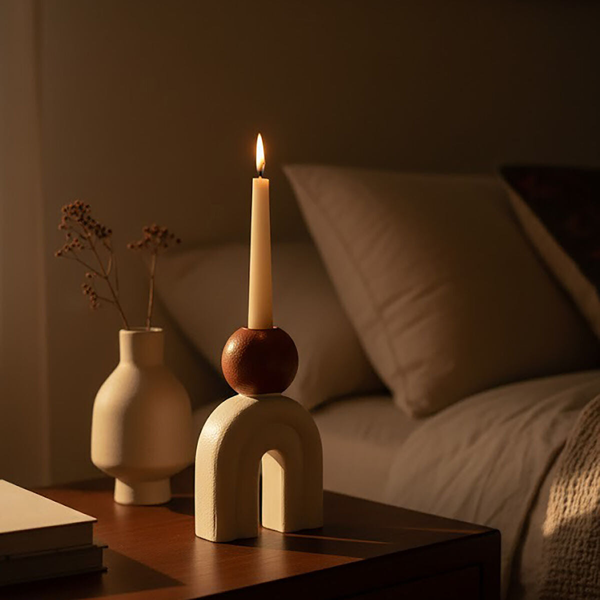 Cream sculptural candle holder with brown accent and single lit taper candle on a side table