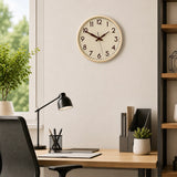 Cream plastic wall clock above home office desk with black lamp and plant