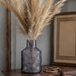 Dark grey textured glass vase with tall dried pampas grass displayed on a wooden table