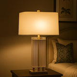Glass table lamp with white shade on bedside table beside sofa