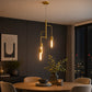 Gold metal pendant light with three exposed bulbs above round dining table