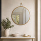 Gold round wall mirror above bathroom shelf with small plant