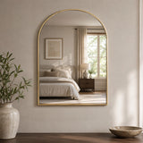 Gold wall mirror above vanity shelf in warm bathroom setting