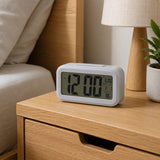 Grey digital clock on wooden bedside table beside neutral bedding