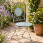 Grey metal outdoor chair with floral seat and scroll back in garden setting