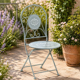 Grey metal outdoor chair with floral seat and scroll back in garden setting