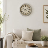Grey plastic wall clock above sofa with neutral cushions and plant