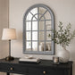 Grey arched wall mirror above console table with lamp and plant