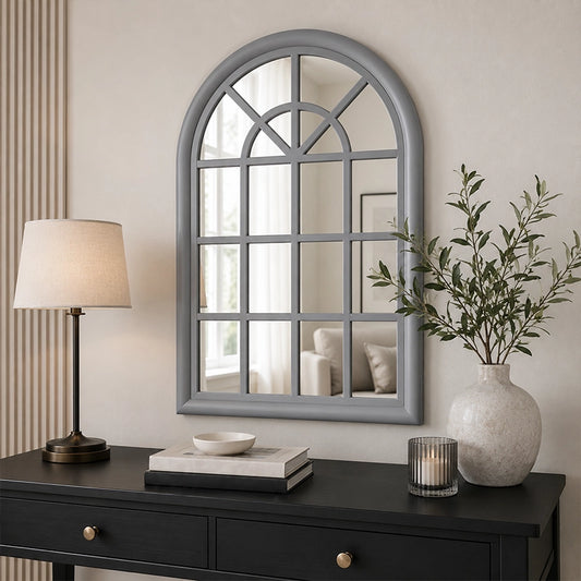 Grey arched wall mirror above console table with lamp and plant