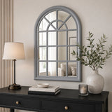 Grey arched wall mirror above console table with lamp and plant