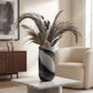 Grey and black decorative glass vase with dark dried foliage displayed on a marble side table